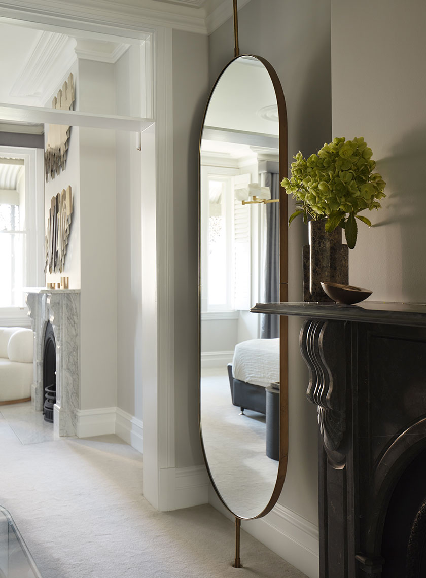 09_Nina-Maya-Residence_K Large Arched Mirror by Fireplace: A tall, arched mirror set above a black mantelpiece, with a vase of green flowers and a glimpse into a luxurious bedroom. Interior design by Nina Maya Interiors at Residence K, Potts Point.