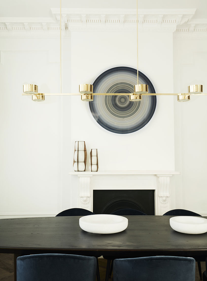 27_Nina-Maya-Residence_K A bright living room featuring a curved gray sofa, a glass coffee table, and green marble side tables, with a backlit art piece on the wall. Interior design by Nina Maya Interiors.