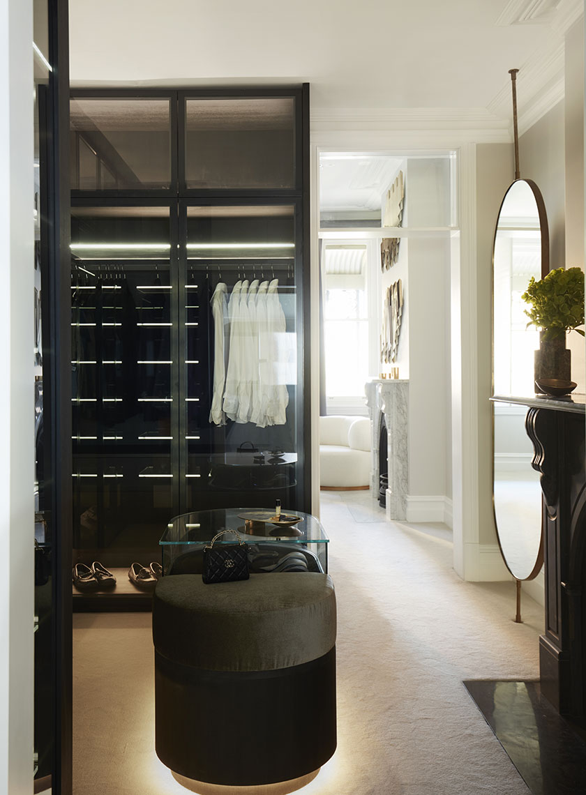 Nina-Maya-Victoria-st2613 Stylish Walk-in Closet with Modern Accents: A chic walk-in closet showcasing a modern display of clothes and accessories behind glass doors, with a large mirror reflecting the elegant room beyond. Interior design by Nina Maya Interiors at Residence K, Potts Point.