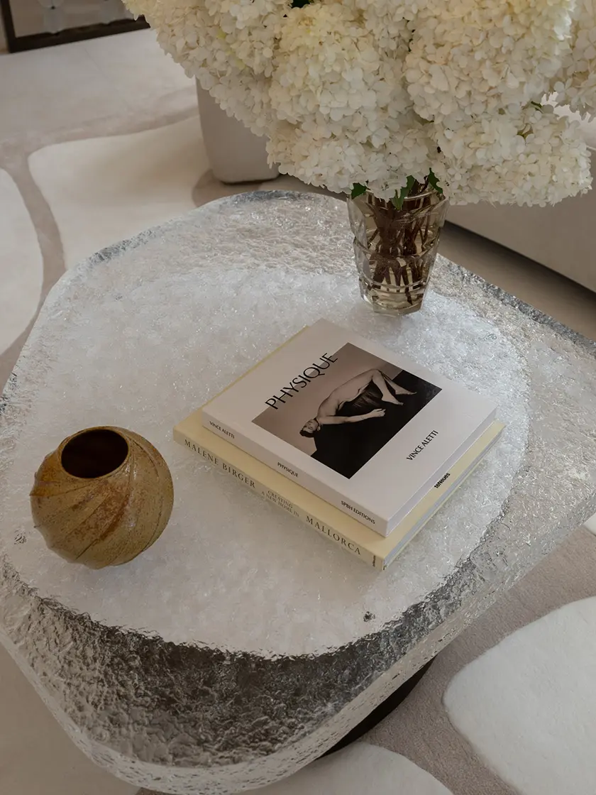Sculptural cast glass coffee tables with dark cylindrical bases in contemporary lounge setting Close-up of textured cast glass coffee table styled with books and floral arrangement